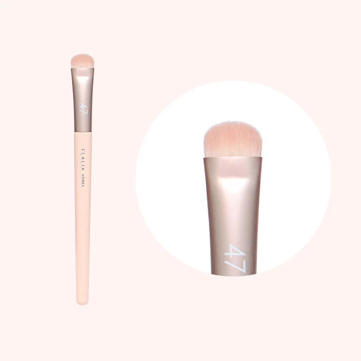A makeup brush with a flat, wide shadow brush head, predominantly beige in color with a metallic silver handle.